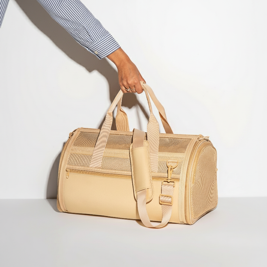 Tan pet carrier held by a person against a white background